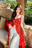 Woman in a red dress and light blue jeans sitting on a stone wall with greenery in the background