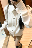Person wearing a white jacket with a chain detail, standing indoors.