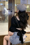 Person wearing a black top with a bow, denim shorts, and a checkered hat in an indoor setting.