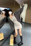 Person wearing a striped sweater and dress, standing in front of a mirror with a shopping bag.