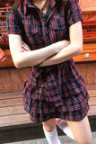 Person wearing a red and black plaid dress with arms crossed, standing against a wooden bench.