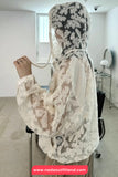 Person wearing a white lace outfit sitting on a chair in a room.