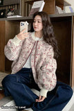 Woman taking a selfie in a floral bomber jacket and jeans sitting on a floor.