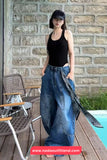 Woman in black tank top and blue jeans standing by a pool with a stone wall background