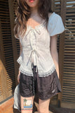Person wearing a white lace top and dark shorts standing in front of wooden shutters.