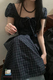 Person wearing a dark plaid outfit with a necklace, sitting indoors.