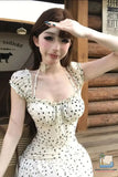 Woman in a polka dot dress posing in front of a wooden wall.