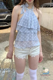 Woman wearing a light blue polka dot halter top and white shorts outdoors.