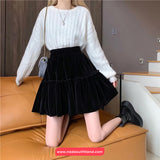 Person wearing a white sweater and black skirt sitting on a brown couch.