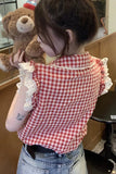Person wearing a red and white checkered shirt with lace trim, holding a brown teddy bear.