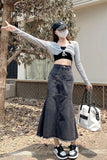 A woman stands outdoors wearing a black and white long-sleeve crop top with a matching black denim fish-neck skirt. She is also wearing a black baseball cap, a white face mask, and carrying a white tote bag.