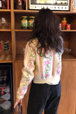 Person wearing a floral sweater in front of a wooden shelf with various items