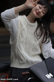 Woman wearing a white cable knit sweater with a blurred background