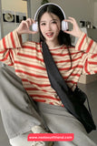 Person wearing a red and beige striped sweater with headphones, sitting indoors.