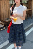 Woman in a white blouse and plaid skirt holding a drink outdoors.