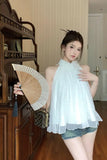 Woman holding a fan indoors, wearing a light blue blouse and denim shorts.