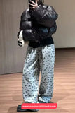 Person wearing a black puffer jacket and light blue floral pants indoors.