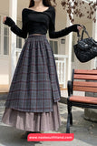 Person wearing a black top and plaid skirt holding a black handbag outdoors.