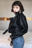 Person wearing a black leather jacket with a belt, standing indoors.