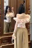 Woman wearing a floral off-shoulder top and beige pants, standing in front of a wooden mirror.