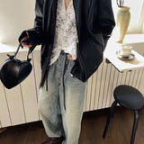 Person wearing a black jacket, white lace top, and light blue jeans in an indoor setting.