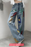 Blue jeans with colorful paint splashes worn by a person on a plain background