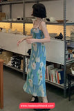 Woman in a floral dress standing in a storage room with shelves and books.