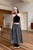 Woman wearing a black halter top and checkered skirt in a room with wooden flooring.