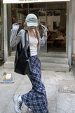 Person wearing a white cap, gray sweater, plaid pants, and white sneakers in front of a store.