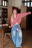 Person wearing a red checkered shirt and blue jeans in a room with wooden furniture and a plant.