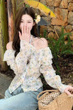 Woman in a floral blouse sitting outdoors with a stone wall and plants in the background