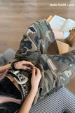 Person wearing camouflage pants with patches, sitting on a wooden floor.
