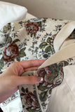 Close-up of a floral-patterned fabric with a hand holding it, on a neutral background.