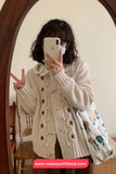 Person wearing a beige cardigan with floral patterns, taking a mirror selfie.