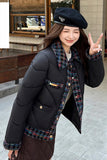 Woman wearing a black puffer jacket with plaid accents and a beret, standing outdoors.
