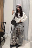 Person wearing a white jacket, plaid pants, and black shoes in a room with a chair and curtain.