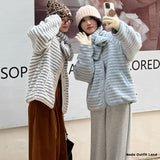 Two people wearing knitted cardigans taking a selfie in front of a store sign.