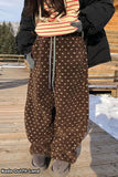 Person wearing brown patterned pants with a black coat and striped shirt on a wooden deck.