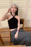 Woman in black top and checkered skirt sitting on a chair indoors.