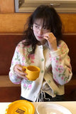 Person wearing a floral sweater holding a yellow mug in a kitchen setting