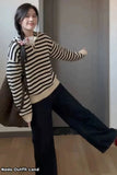 Woman wearing a striped sweater and black pants posing indoors.