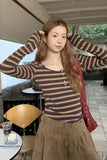 Woman wearing a striped sweater and brown pants outdoors with a blurred background