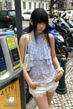 Woman in a polka dot top and white shorts standing next to a parking meter on a street.
