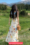 Woman in a floral dress standing in a grassy field with mountains in the background