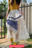 Person wearing a yellow top and white skirt with blue accents, standing outdoors.