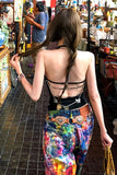 Woman in colorful pants and open-back top walking through a market.