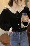 Person wearing a black velvet blouse with lace collar and cuffs, holding a glass of wine.