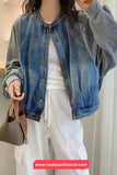 Person wearing a denim jacket and white pants, holding a brown handbag indoors.