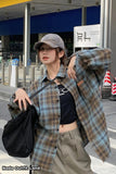 Person wearing a plaid shirt over a black crop top with a gray cap and beige pants, standing outdoors.