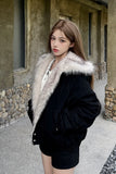 Woman wearing a black coat with fur trim standing in front of a stone building.